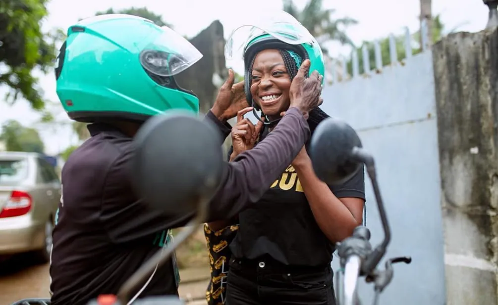 Motorcycle rider in teal helmet helps smiling female passenger adjust her matching helmet before a ride