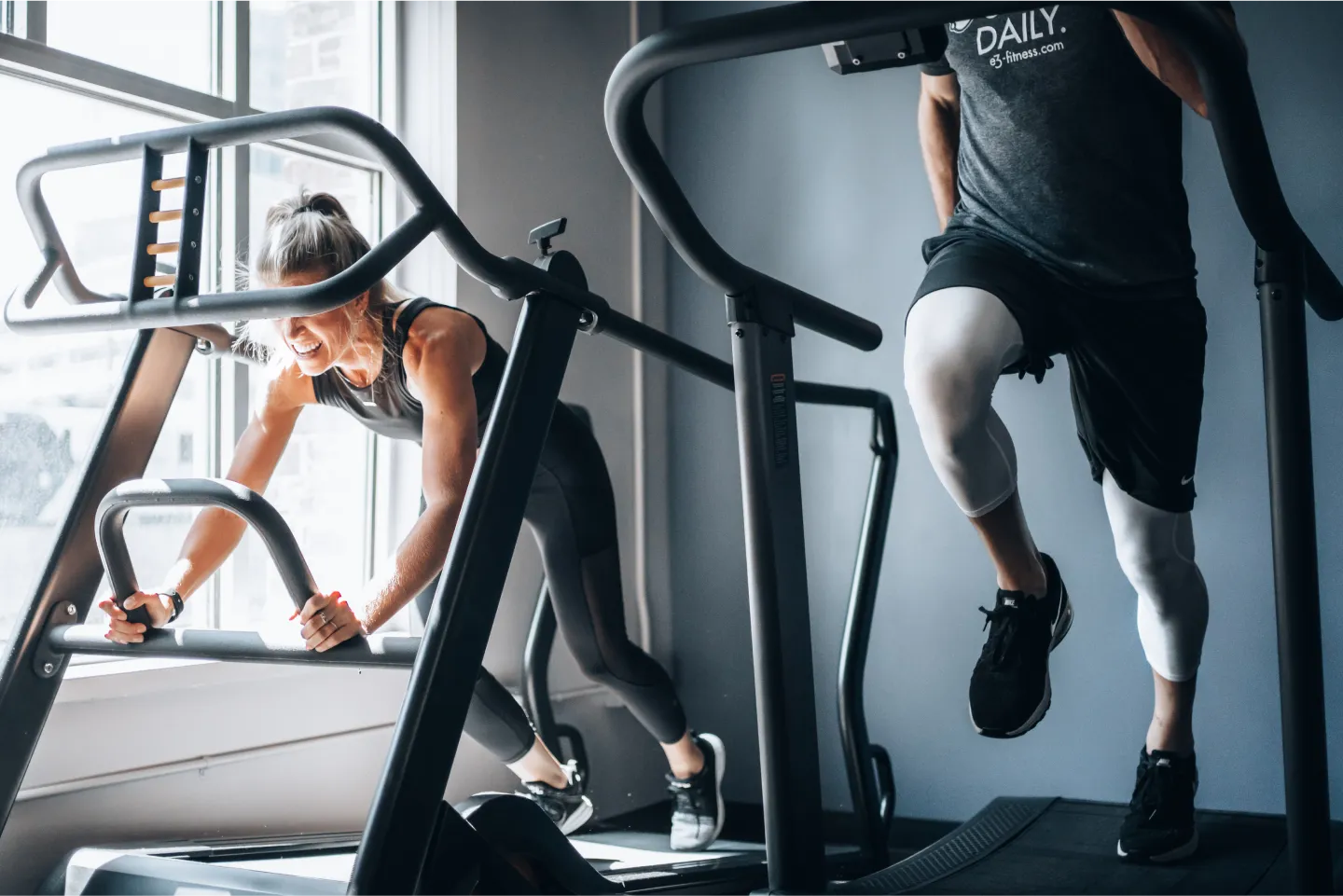Two people intensely running on steep incline treadmills in a gym