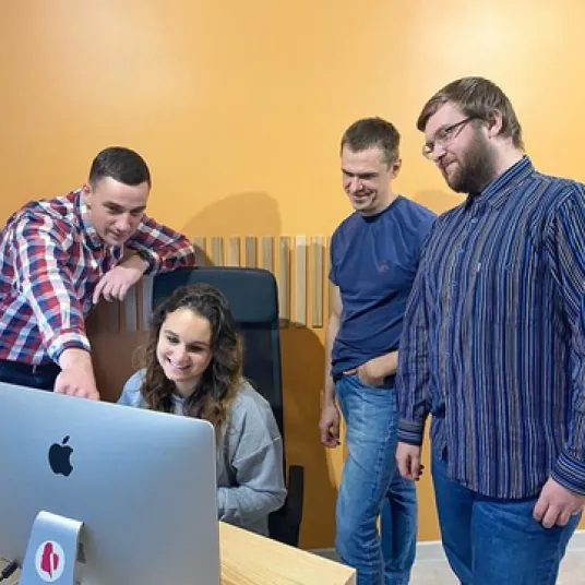 Four people gathered around an iMac in a room with orange walls