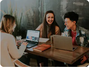 Three smiling students siting in cafe with laptops