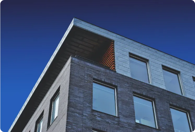 Low-angle view of a modern brick building with large glass windows against a deep blue sky