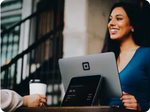 Smiling woman with long dark hair in blue top at outdoor cafe table siting with tablet near man