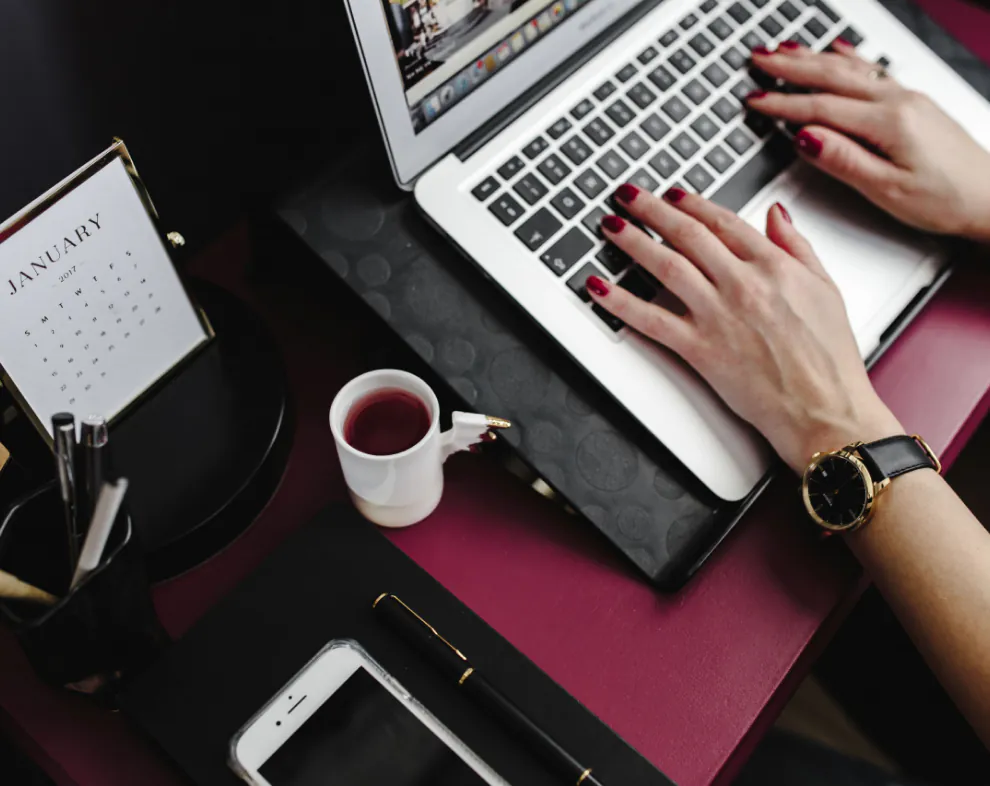 Person typing on laptop at desk with coffee, phone, pen, and January calendar